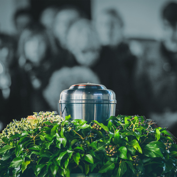 A silver urn among green flowers with a blurred crowd in the background