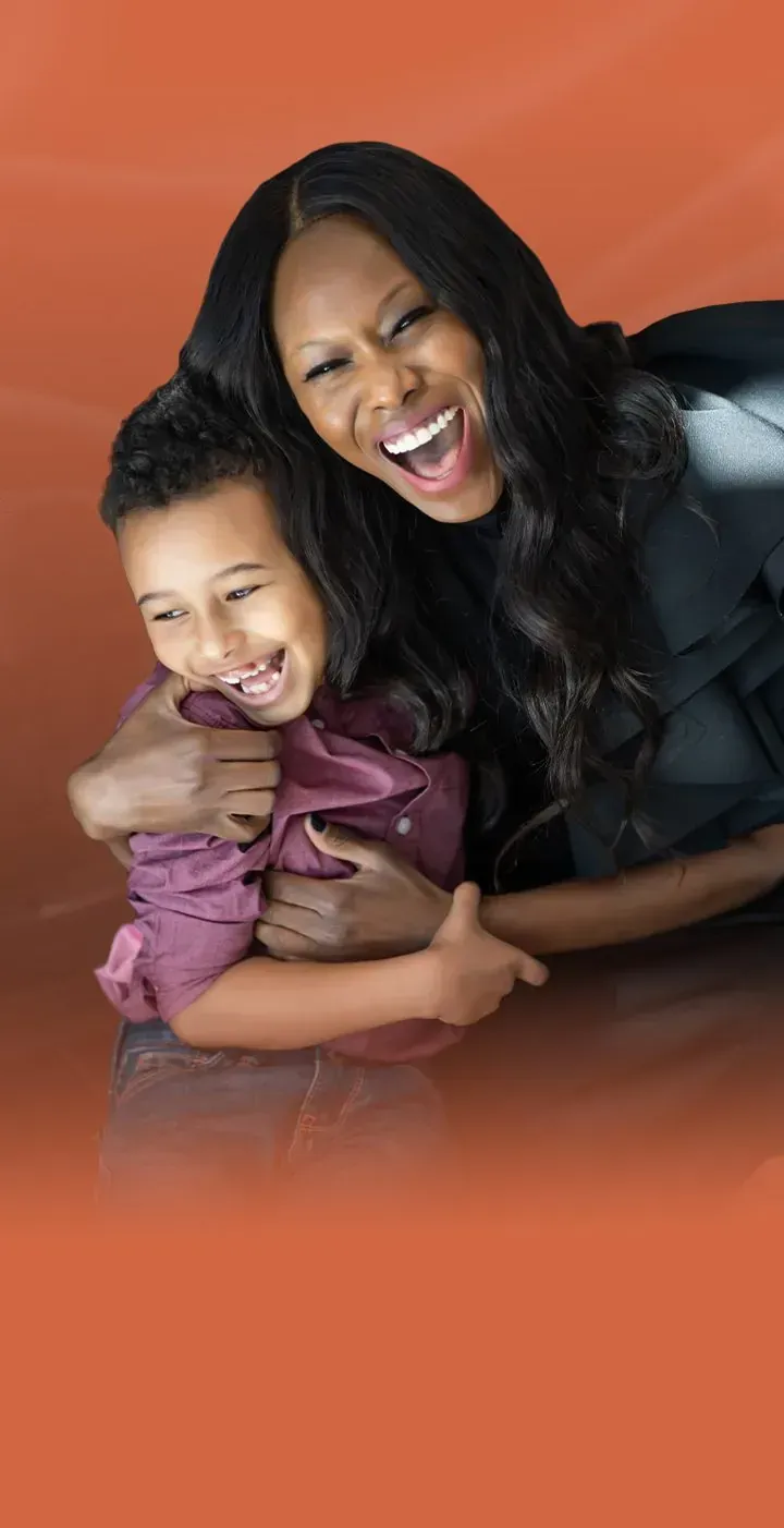 Rosebell Murigu smiling and hugging against an orange background