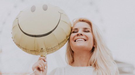 Smiling blonde woman holding a gold balloon against a light background