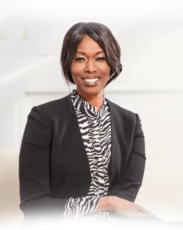 Portrait of Rosebell Murigu in a black blazer and patterned blouse against a bright white background