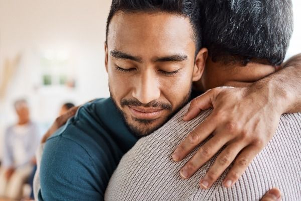 a man is hugging another man with his eyes closed .