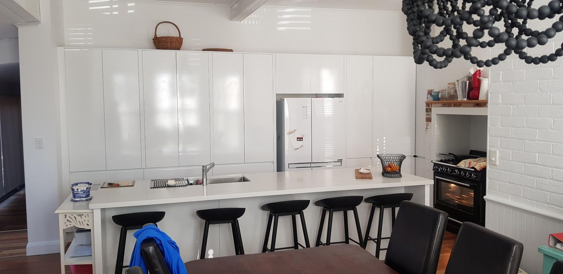 A Kitchen With White Cabinets, Stools, a Table and a Refrigerator — Kareela Constructions In Tamworth, NSW