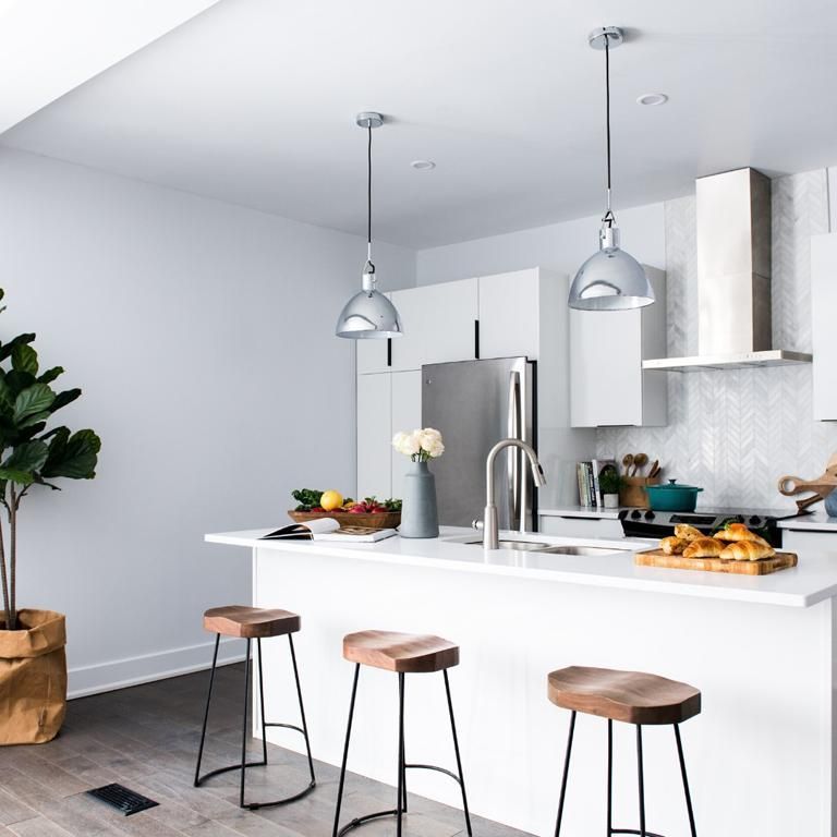 A White Kitchen With Hanging Lights And Bar Stool Seats
