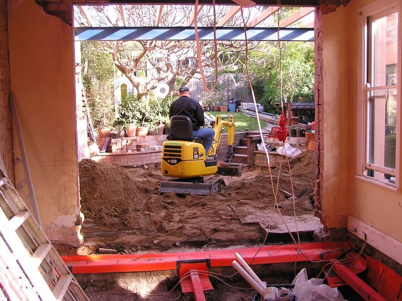 A Man is Driving a Small Yellow Excavator in a Garage — Kareela Constructions In Tamworth, NSW