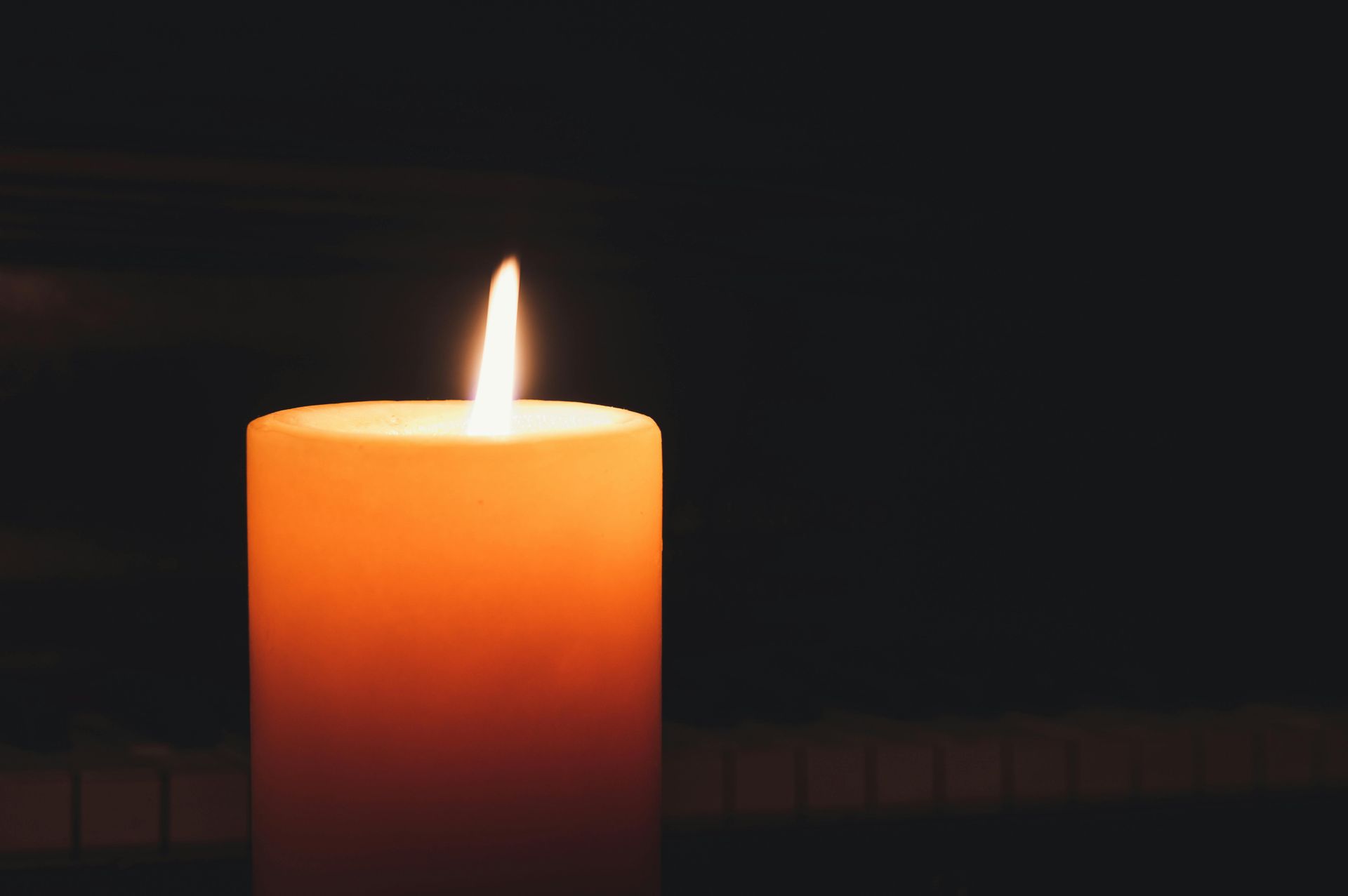 Lit orange candle against a dark background, with piano keys subtly visible.