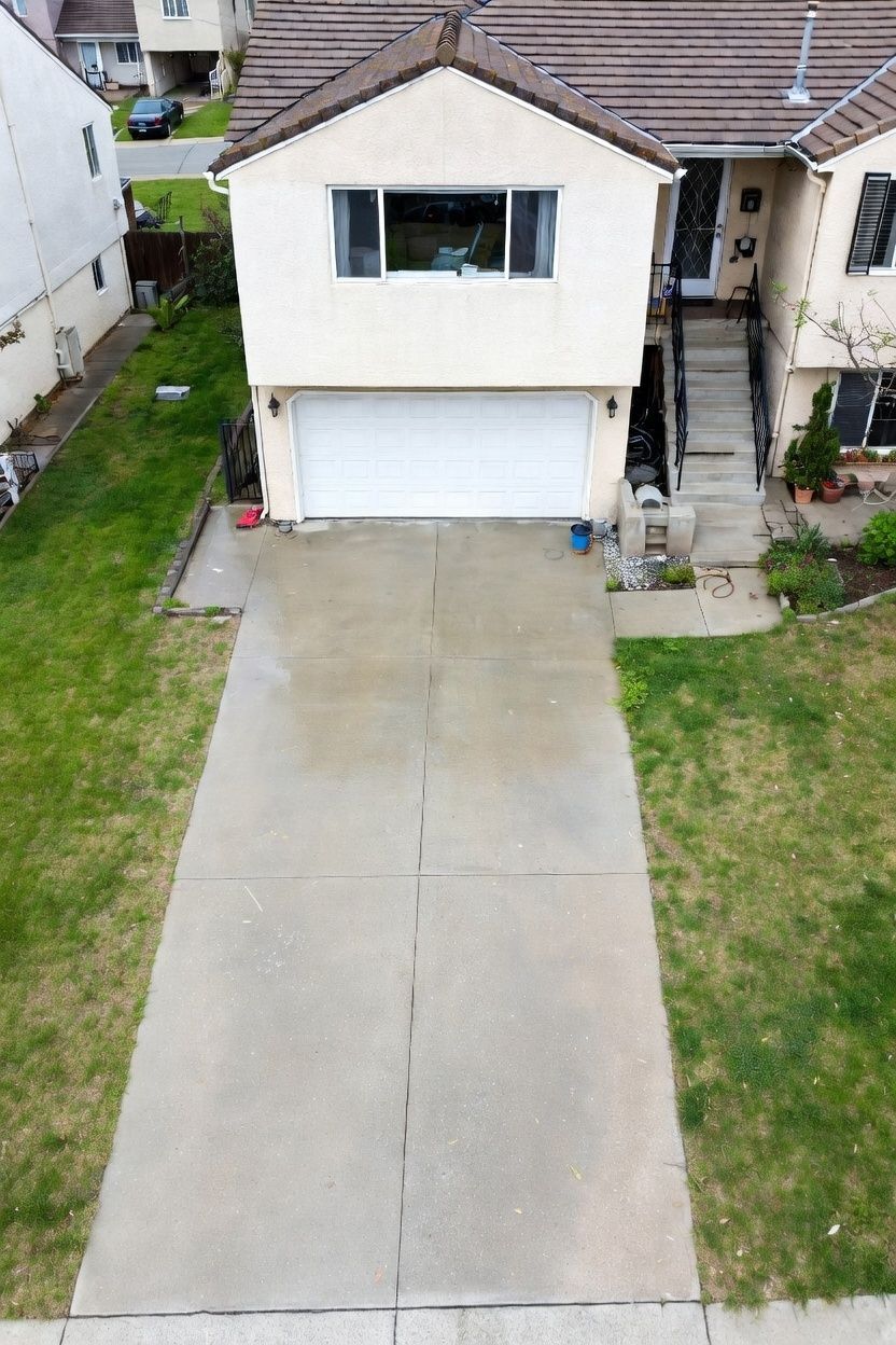 A high-angle view of a cream-colored house with a single-car garage and a concrete driveway surrounded by green lawn.