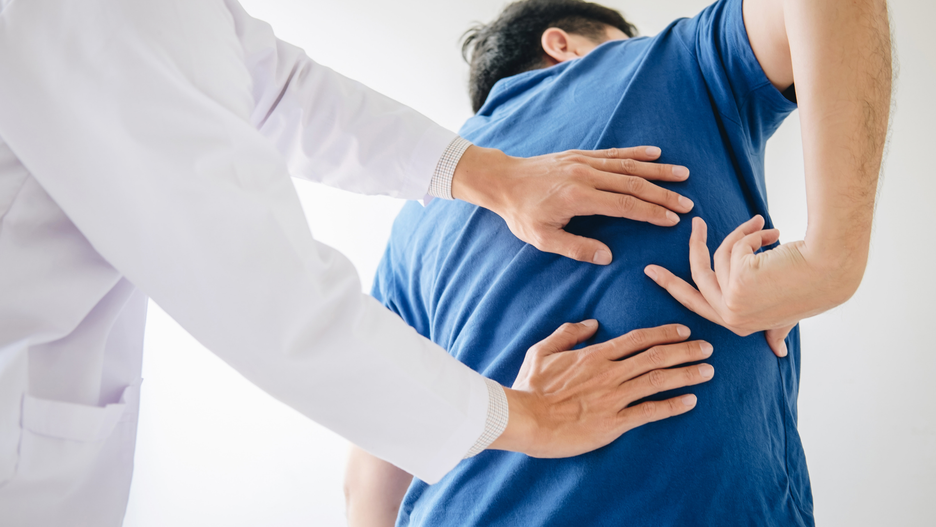 Healthcare worker examining a patient’s lower back with hands on the spine area