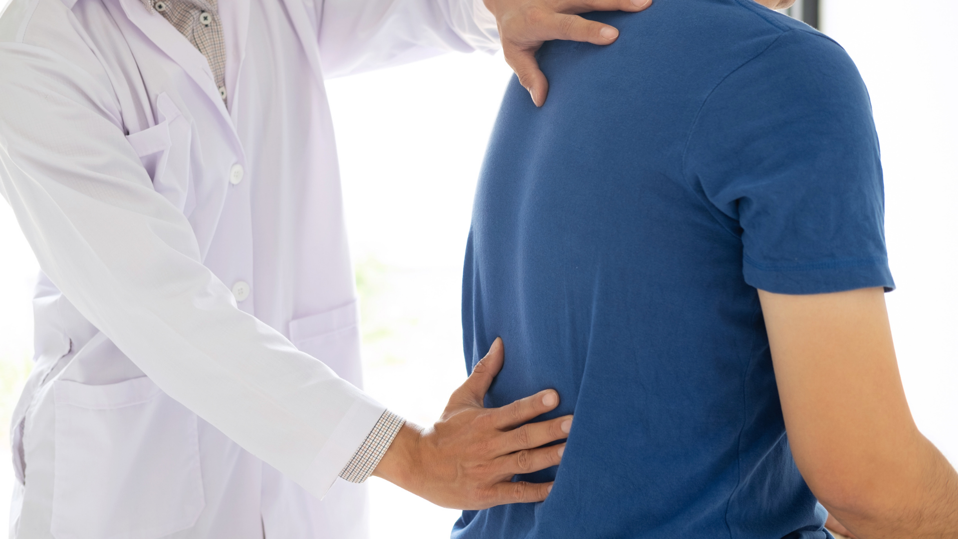 Doctor examining a patient’s back and neck, with hands placed on the shoulder and lower back.