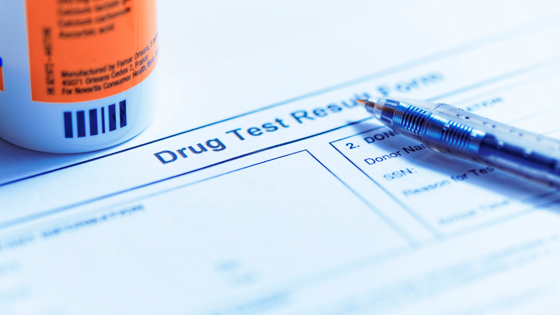 Drug test form with a pill bottle and pen on a desk