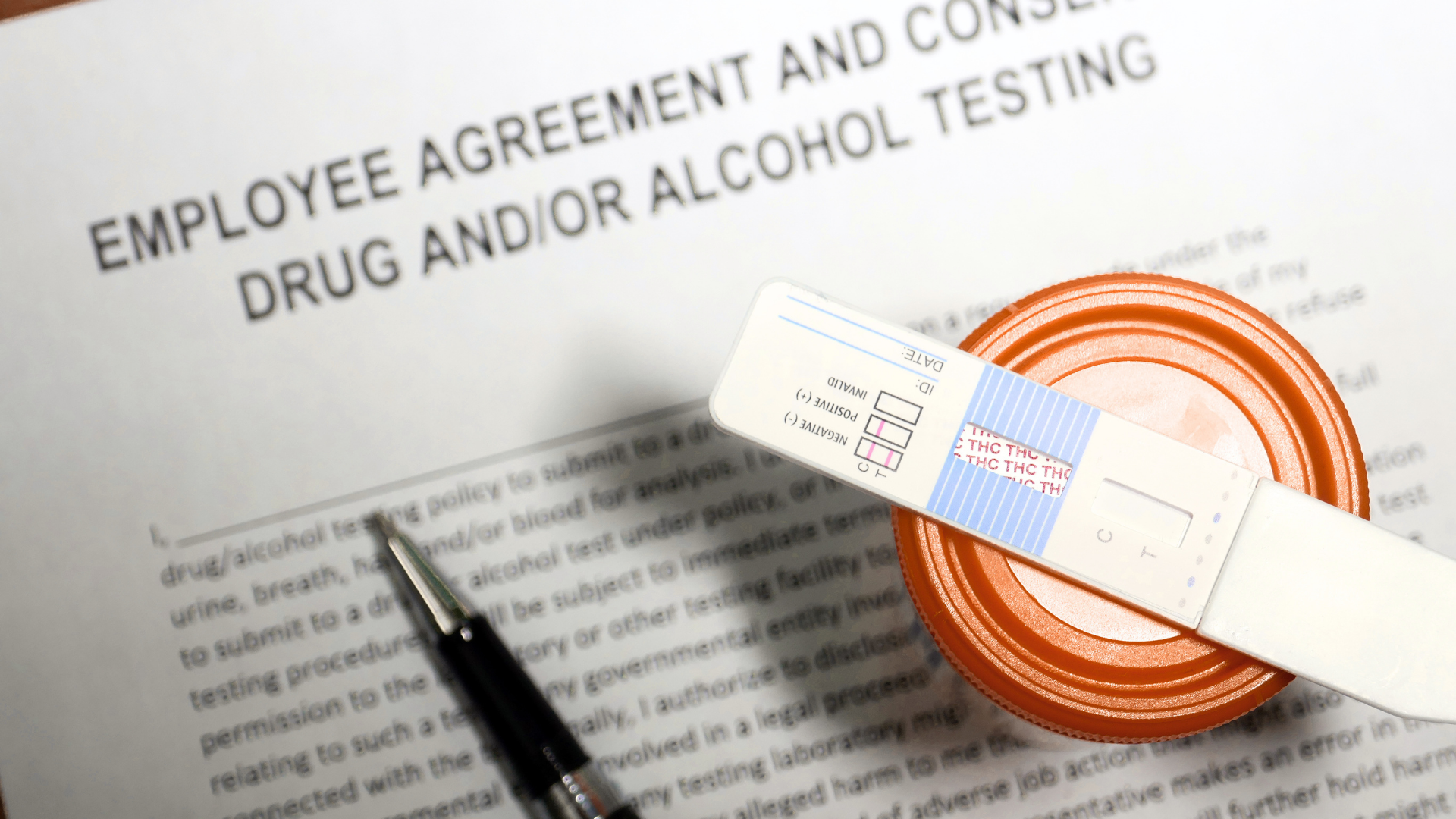 Drug and alcohol testing agreement form with pen and a sealed sample device on top