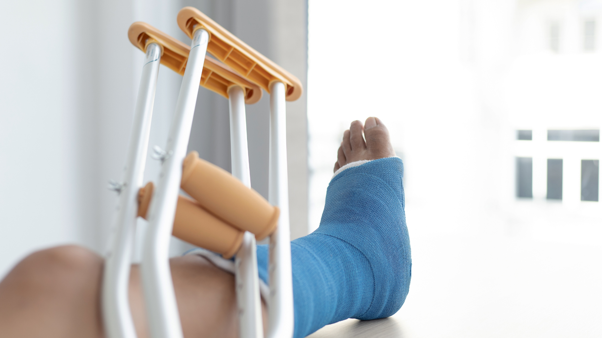 Person’s foot in a blue cast resting on crutches by a bright window