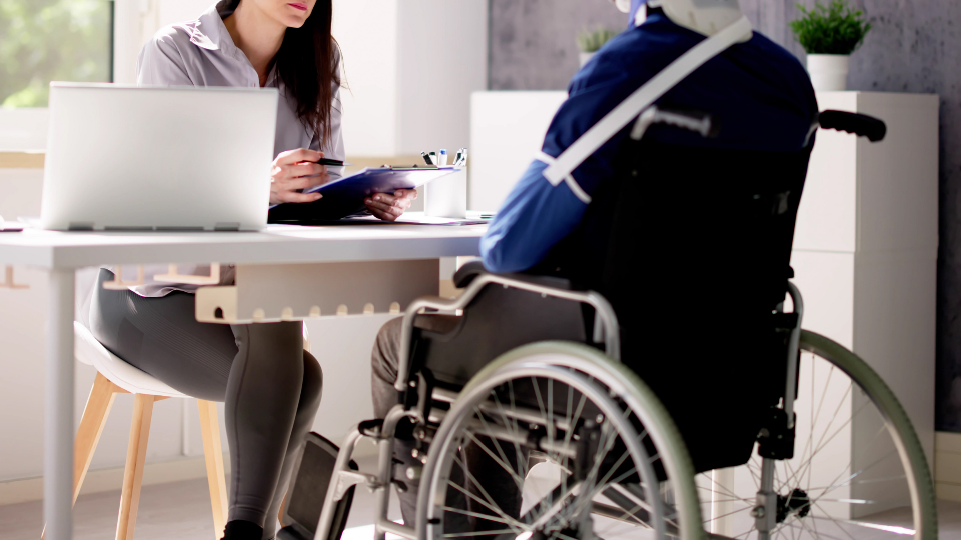 Person in a wheelchair speaking with a woman at a table in a bright office