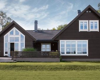 Moderne hus i mørkt tre med store vinduer og en liten veranda foran under en blå himmel