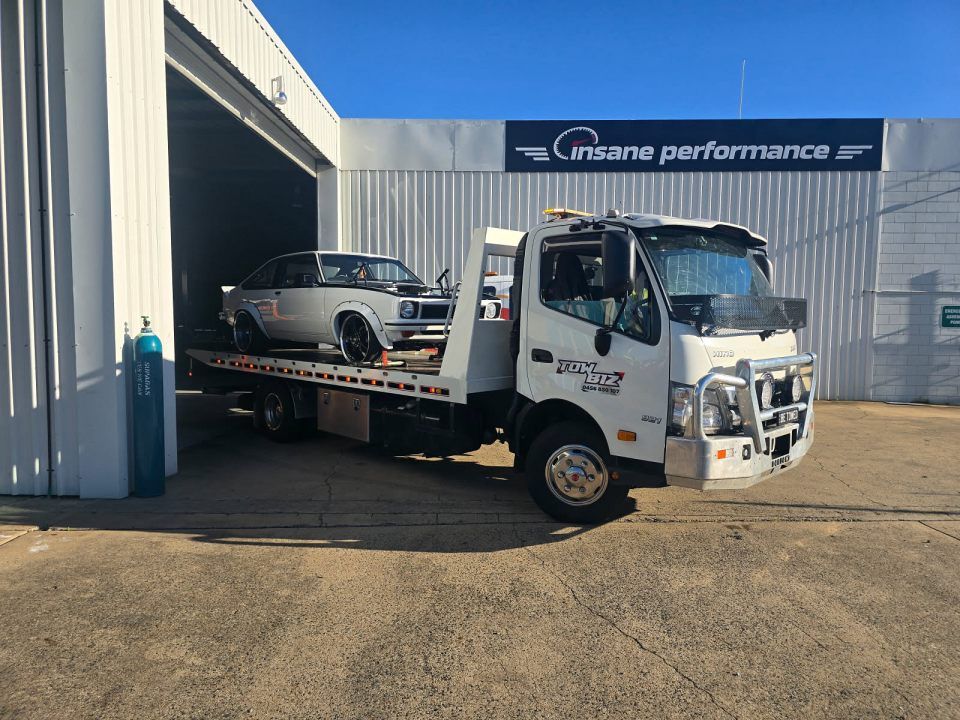 A Tow Truck With a Car on the Back is Parked in Front of a Garage — Tow Biz in Emu Park, QLD