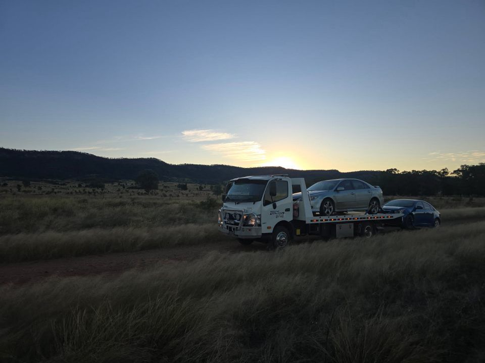 Two Cars Are Being Towed by a Tow Truck in a Field at Sunset — Tow Biz in Park Avenue, QLD
