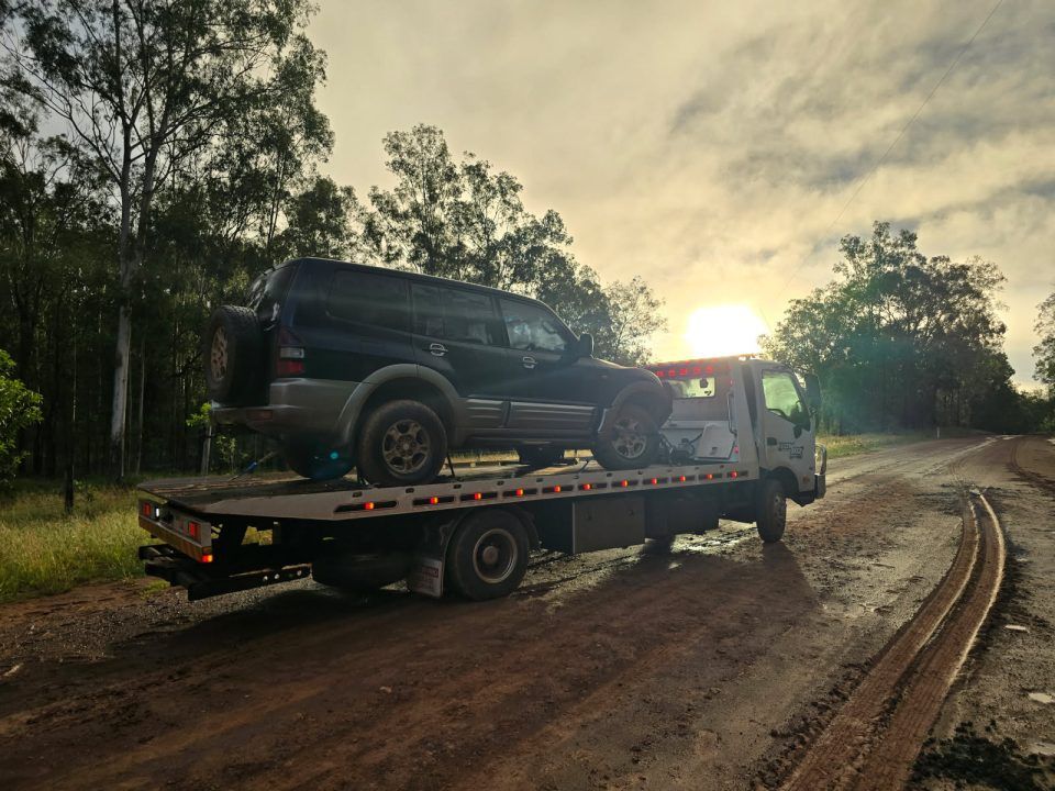 A Black Suv is Being Towed by a Tow Truck on a Dirt Road — Tow Biz in Biloela, QLD