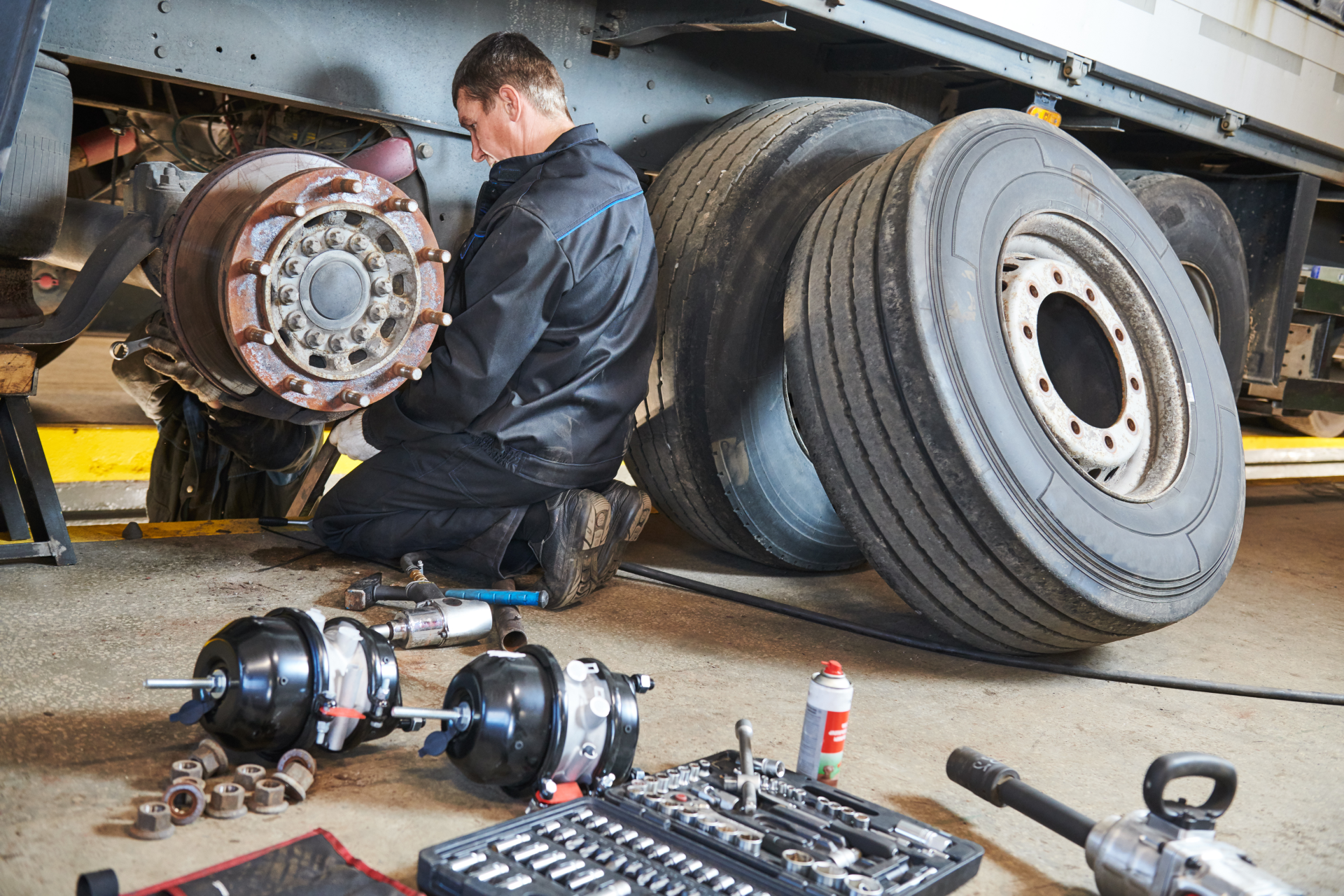 Mechanic replacing brakes on a semi-truck tire. Tools, tires, and brake components are in a garage.