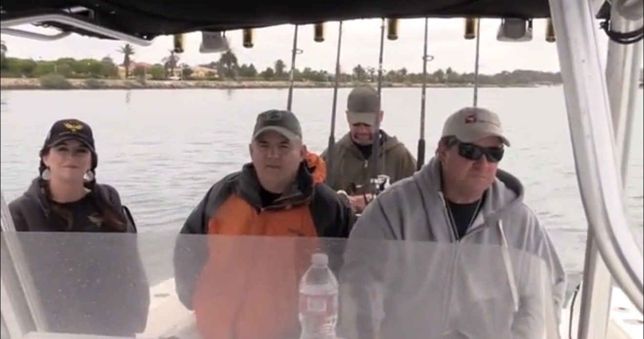 Four people on a boat, fishing rods visible, cruising on water.