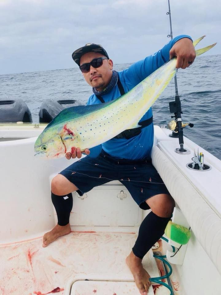 A person in a blue shirt and sunglasses holding a large, bright yellow-and-green mahi-mahi on a boat.