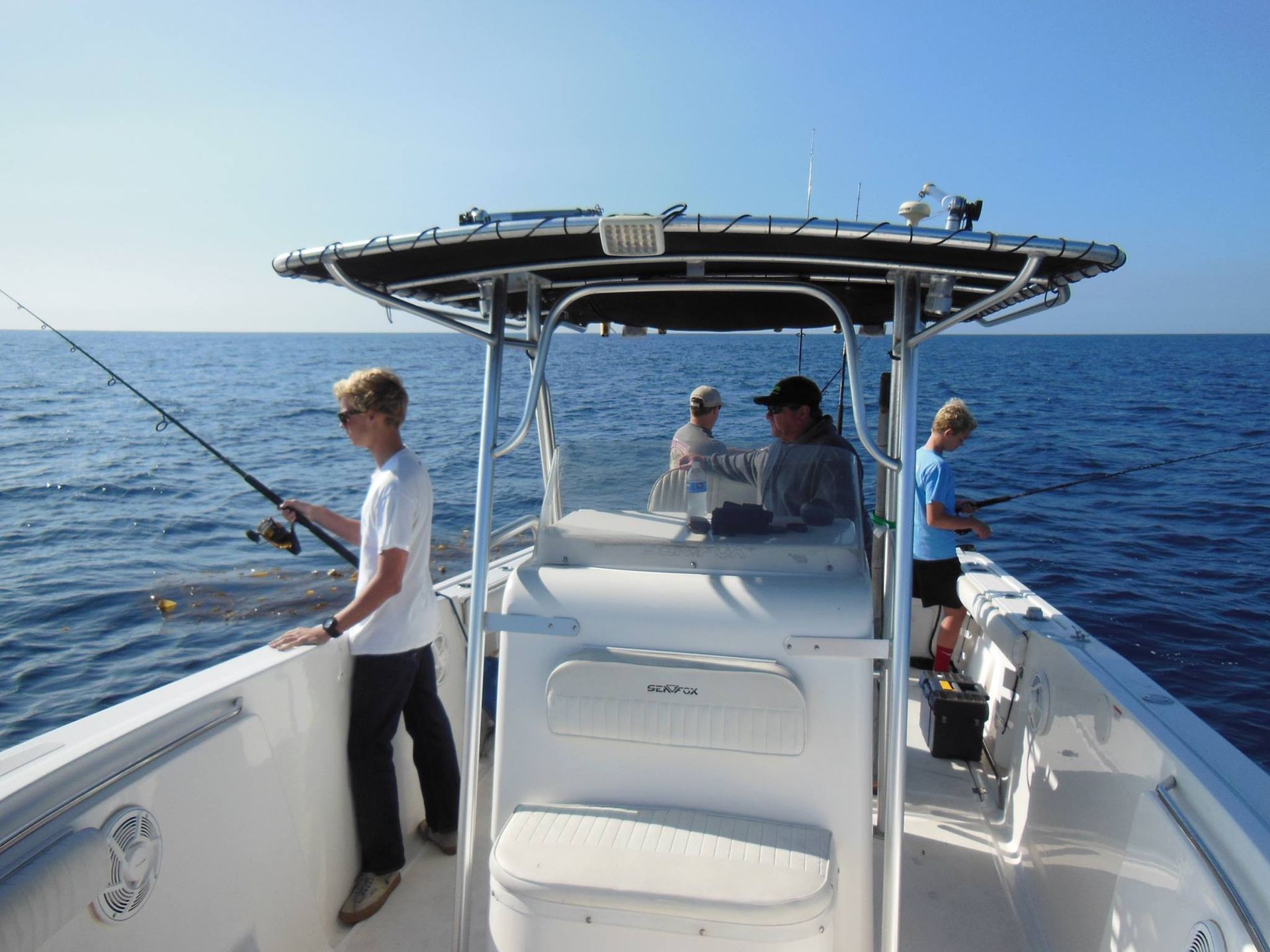 Three people fishing from a boat on a vast, blue ocean under a clear, bright sky.