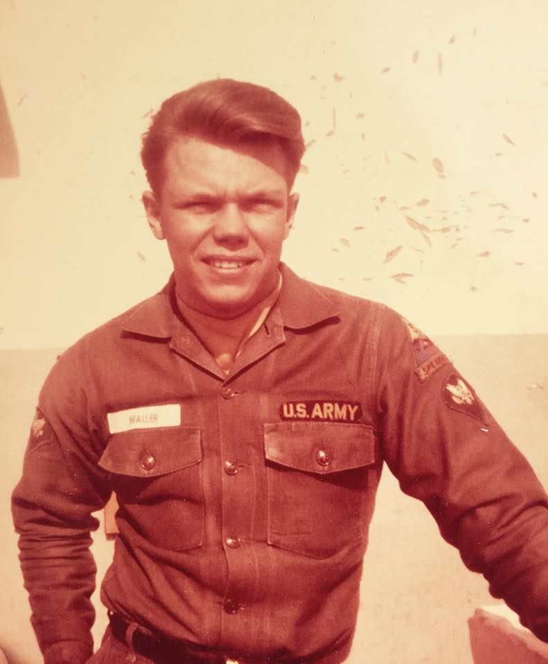 A soldier in a tan uniform with U.S. Army insignia standing against a light background.