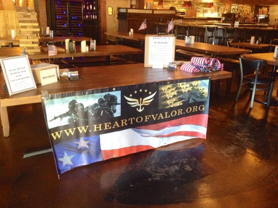 A Heart of Valor table display featuring a banner with soldiers, a flag motif, and the website URL in a restaurant setting.