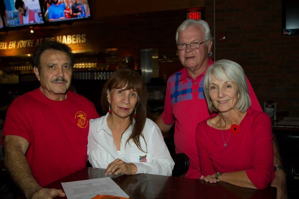 Four adults stand together at a bar table, smiling for a photo in a dimly lit restaurant.