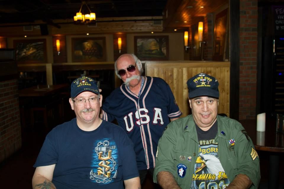 Three people in patriotic attire pose for a photo inside a dimly lit restaurant.