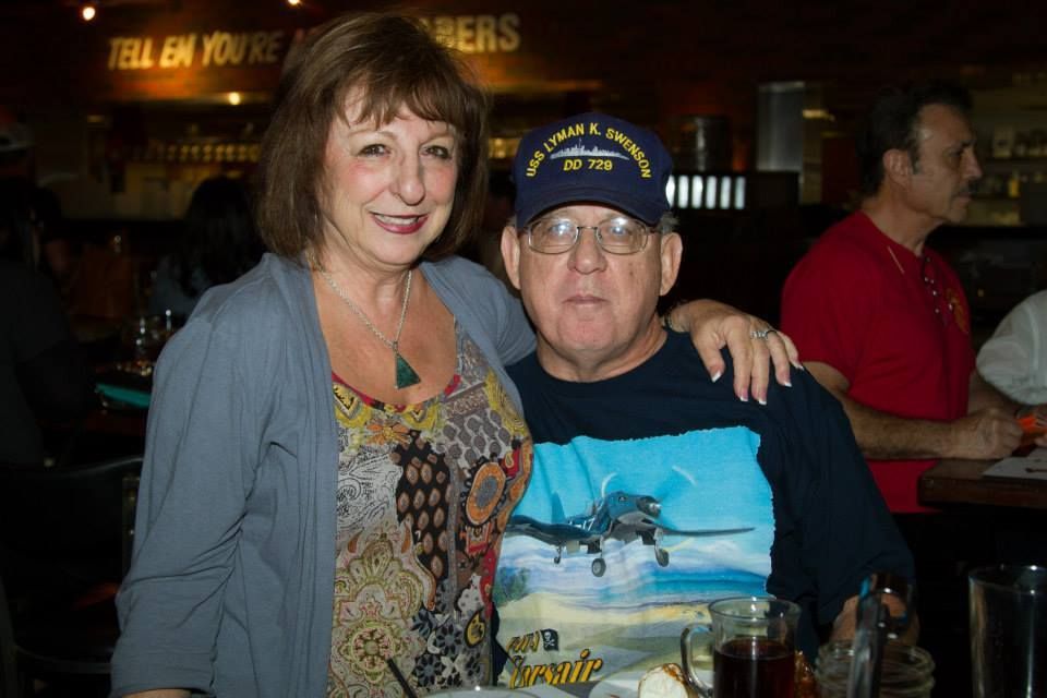 A woman and a man in a navy baseball cap pose together for a photo in a dimly lit restaurant.