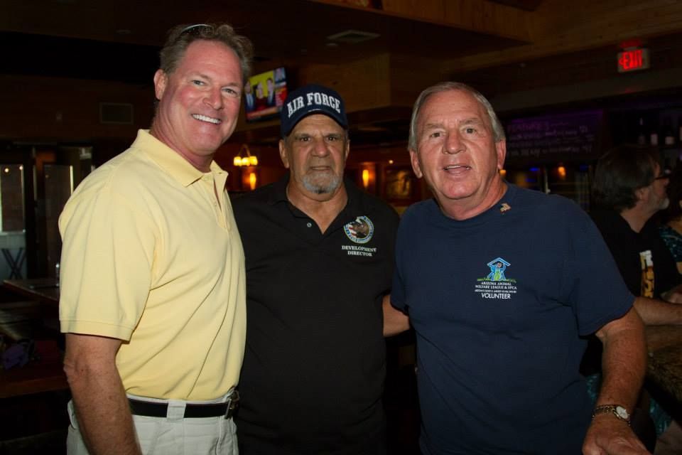Three men pose for a photo in a dimly lit restaurant, wearing casual shirts and smiling at the camera.