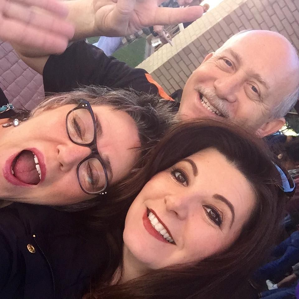 A selfie of three people smiling and posing closely together against a brick background.