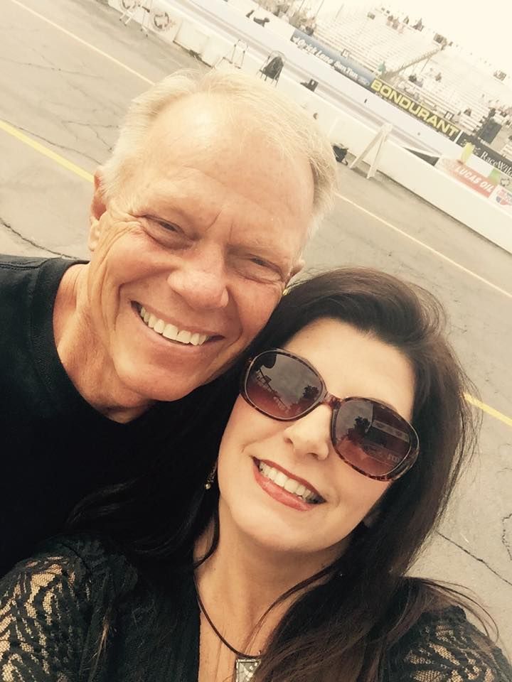 A smiling couple poses for a selfie at an outdoor race track.