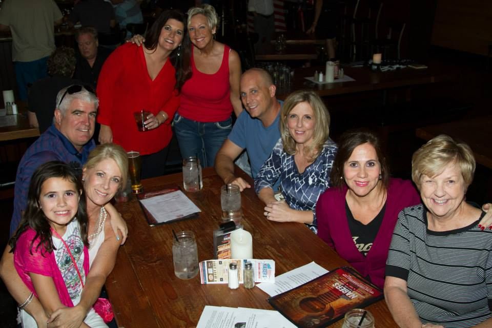 A diverse group of ten people sitting around a long wooden table in a restaurant, smiling and talking.