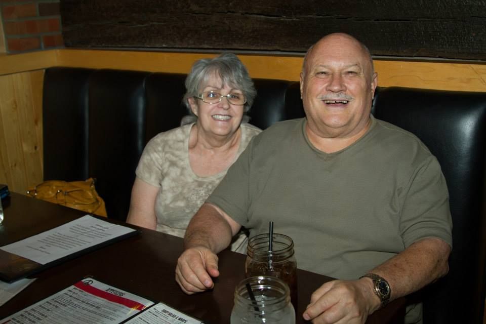 Two people smiling while sitting at a restaurant booth with menus and drinks on the table in front of them.