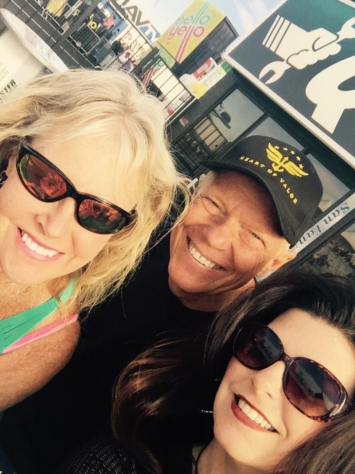 Three people smiling closely together in a selfie outdoors near a sign with a logo.