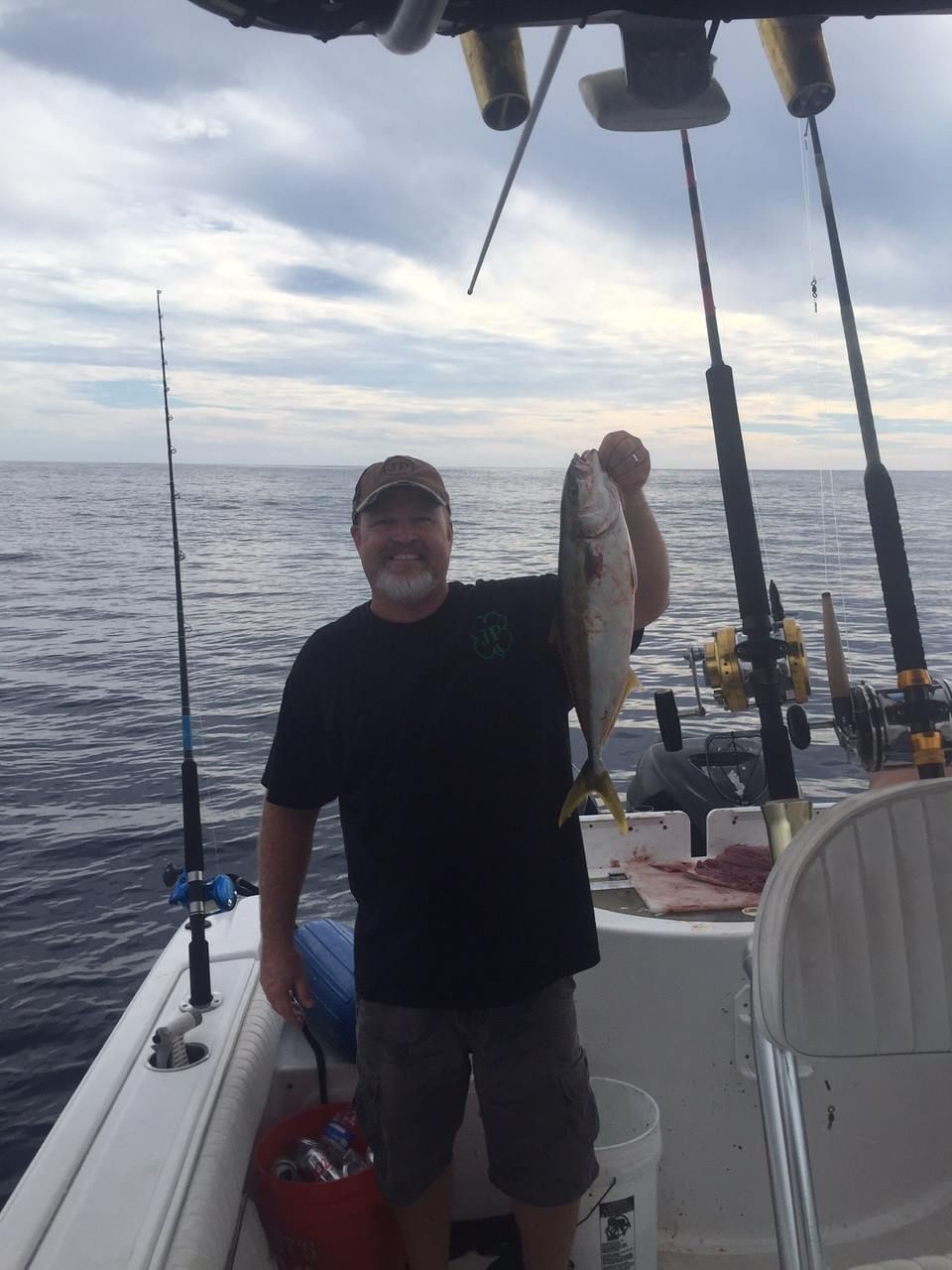 Man on a boat, holding a caught fish with fishing rods in the background, cloudy sky.