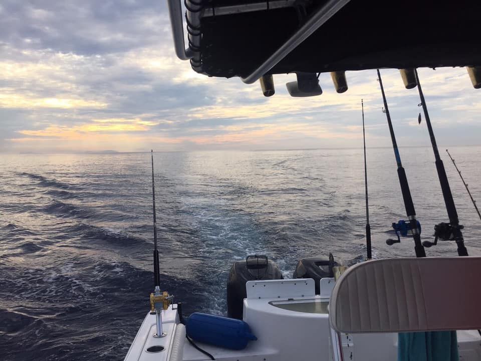 A view from the stern of a boat looking out at the open ocean under a cloudy sky at sunset, with fishing rods set up.