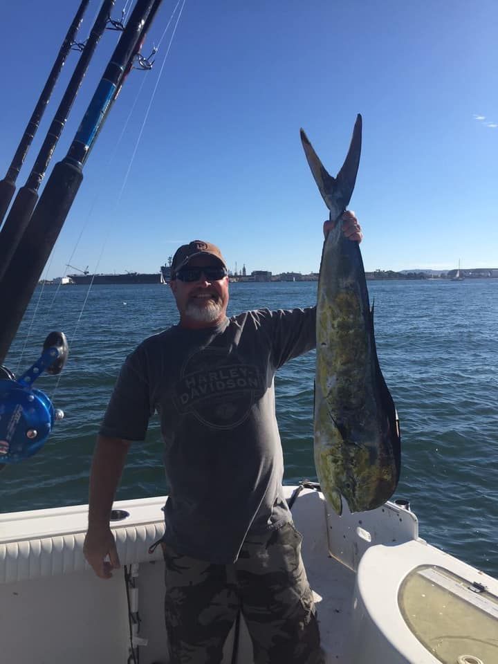 A person smiling while holding up a large mahi-mahi fish on a boat on a sunny day.