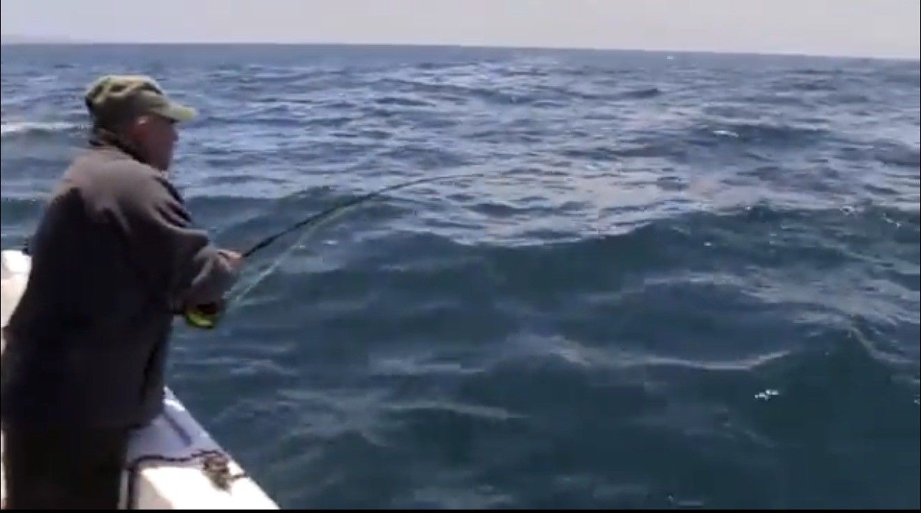 Man fishing from a boat in choppy blue water, holding a fishing rod.