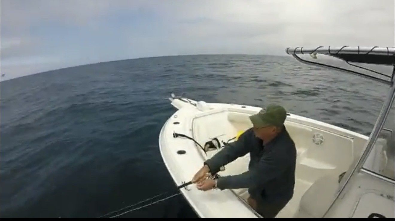 Man on a white boat pulling a rope, on the open ocean under a cloudy sky.
