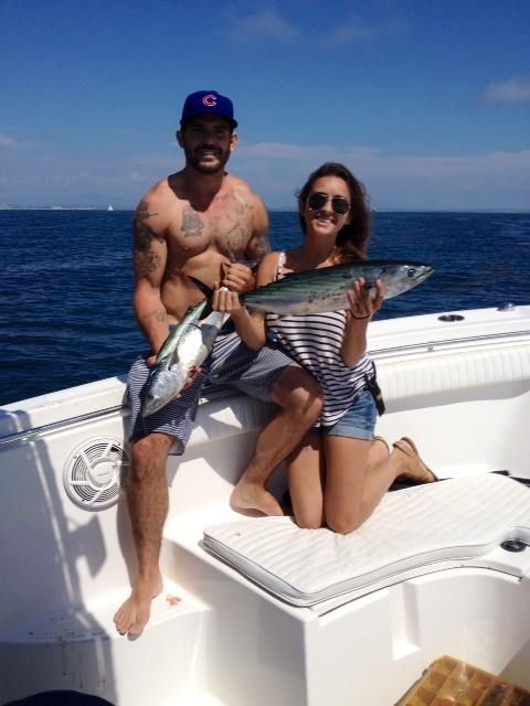 Man and woman on a boat hold up fish they caught. Sunny day, blue water, boat.