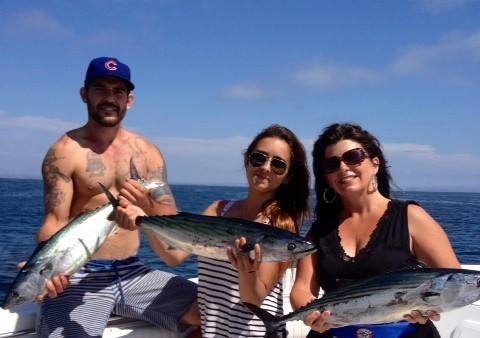 Three people on a boat display their freshly caught fish against a blue sky and ocean background.