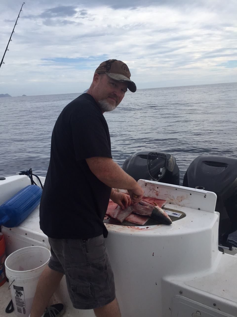 Man cleaning fish on a boat at sea. He is wearing a cap and black shirt.