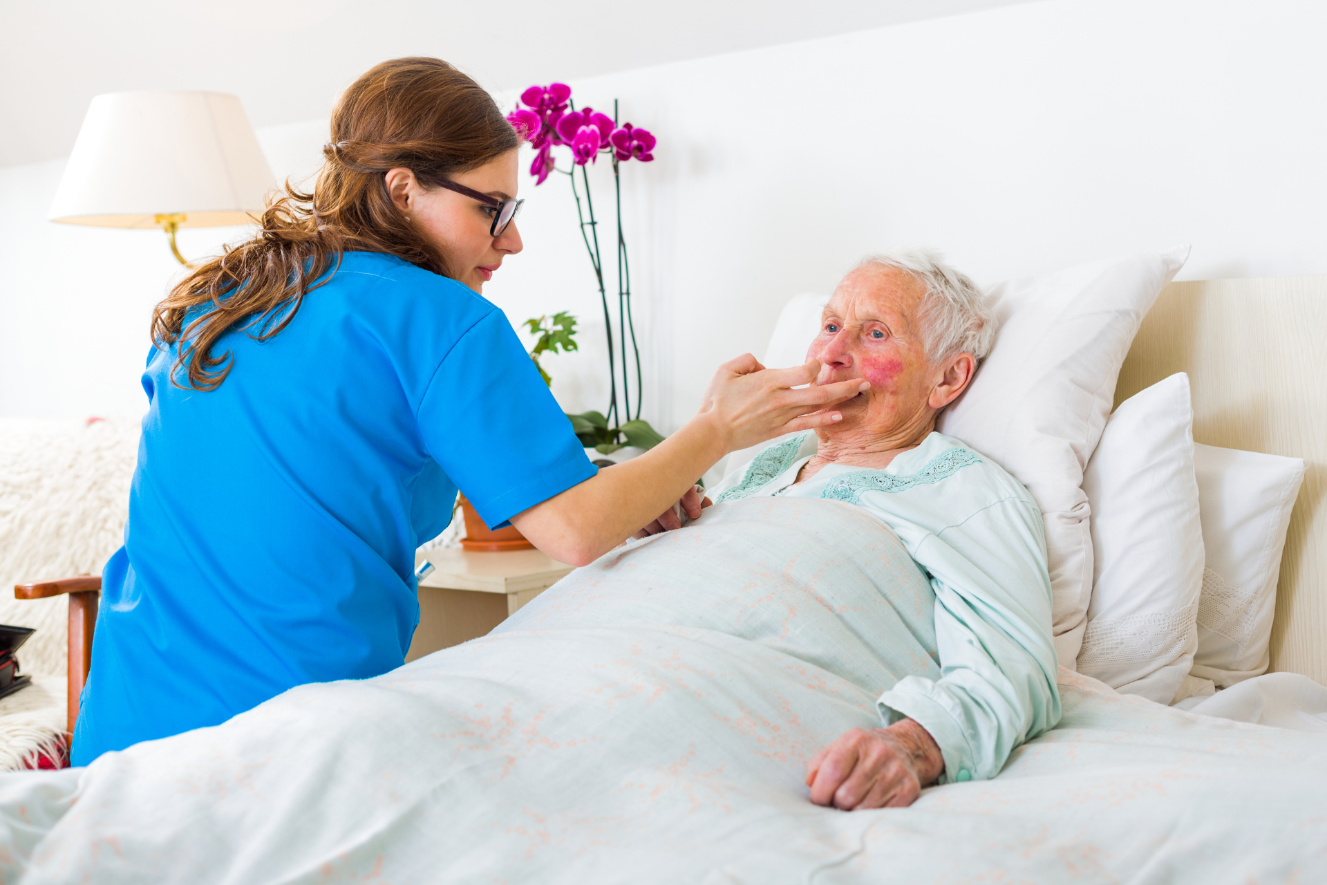 Caregiver feeding an elderly patient in bed with a spoon in a bright bedroom