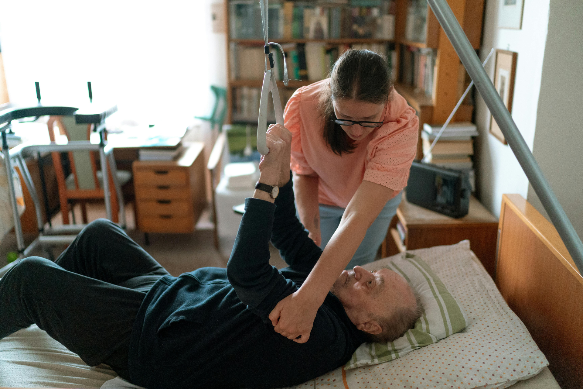 Caregiver assisting a patient with a leg stretch in a home bedroom