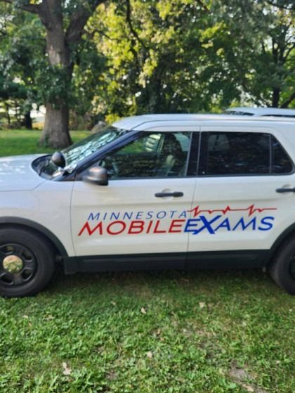 White SUV with Minnesota Mobile Exams logo parked on grass near trees