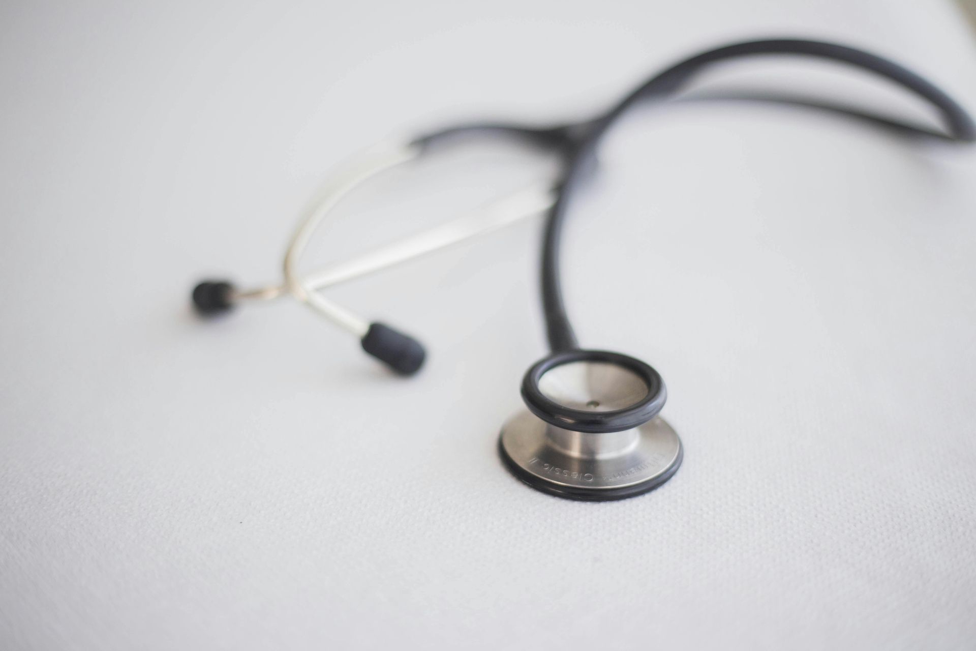 Stethoscope on a white surface, black tubing and silver chest piece in close-up.