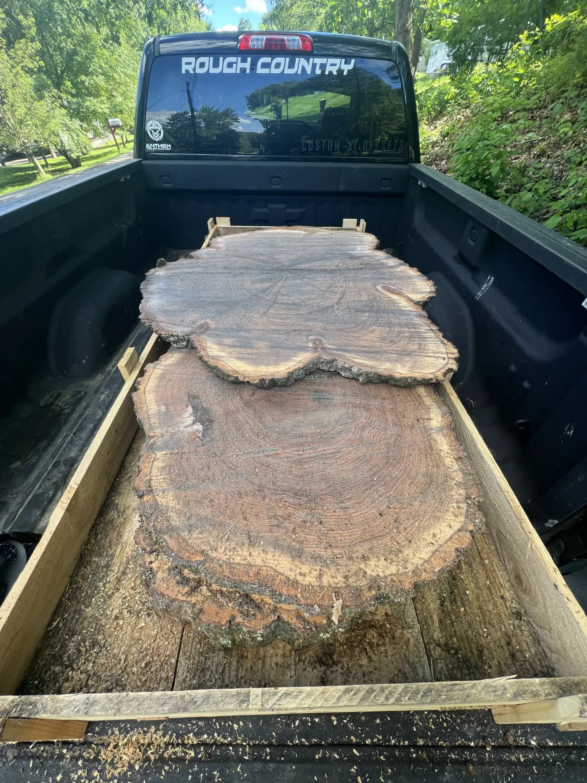 Pickup truck bed loaded with large cut tree trunk sections in an outdoor setting