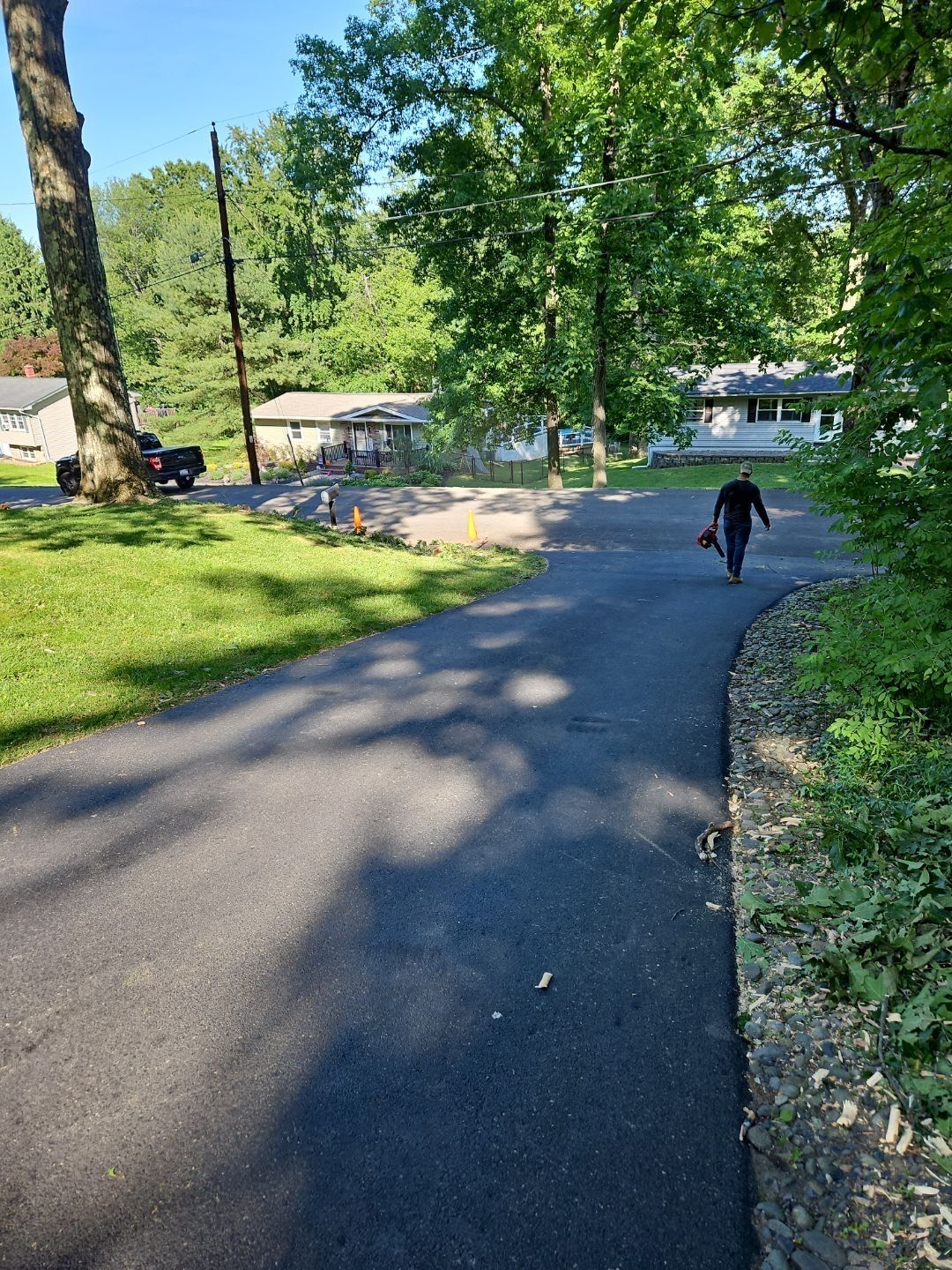 Wooded park path curving downhill past a person walking toward houses in the distance