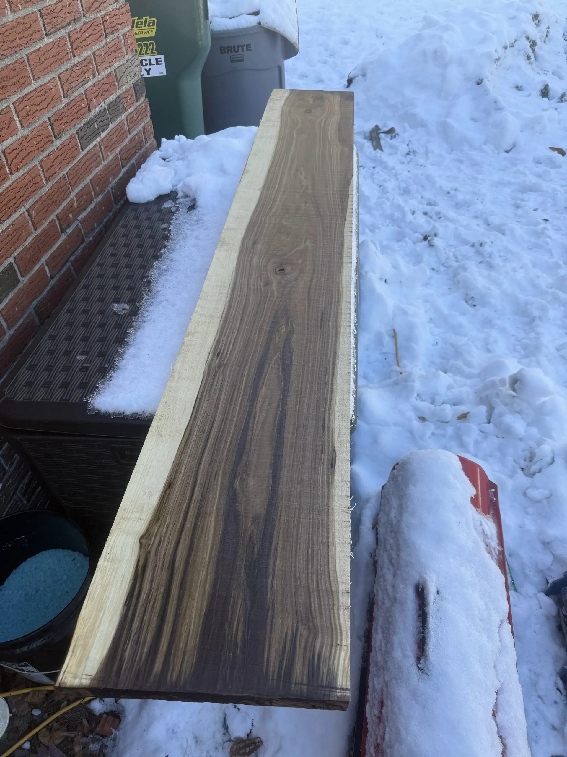Long wooden plank resting on snow beside a brick wall and steps
